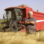 man standing in a field of wheat with combine
