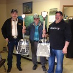 three men holding award in shape of a shovel