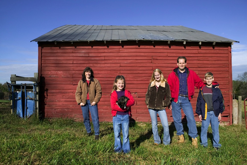 Family portrait standing in front of a red barn on the farm.