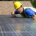 Young maintenance worker installing solar panels on rooftop