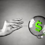 A hand about to burst a money bubble with a pin. Metaphor for an economic or financial bubble crisis.