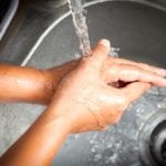 Woman washing her hands under running water in kitchen room