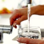 Woman Pouring Glass Of Water From Tap In Kitchen