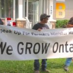Members of Grain Farmers of Ontario sport a banner outside a provincial cabinet minister’s office in 2015. (File photo by Ralph Pearce)