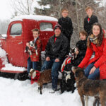 Even though they’re staying at home these days, life on the Taylor farm is pretty busy. Far left is William (holding Fetchy LaRue), Mark (with Meeps, a bottle-fed baby goat), Elias, Nathan (with Finn), Jacob, and Tamara (with Allen and Gilbert).