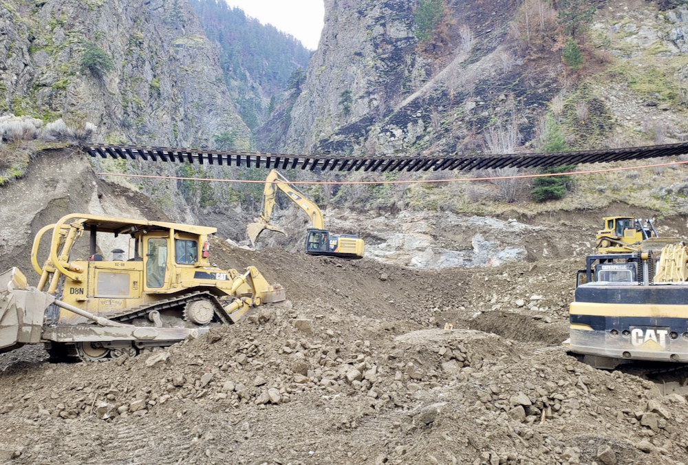 Crews work to shore up a section of railway that hangs in mid-air after the ground below was washed away by flooding.