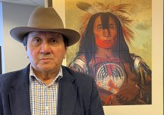 Kainai-Blood Chief Roy Fox (Blackfoot name Makiinima) stands in front of a painting of Stamikso’sak, a Blood Tribe war chief from the early 1800s.