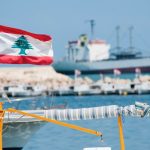 File photo of a small boat flying the Lebanese flag at a marina in Tripoli as a cargo vessel sails in the distance. (Joel Carillet/iStock/Getty Images)