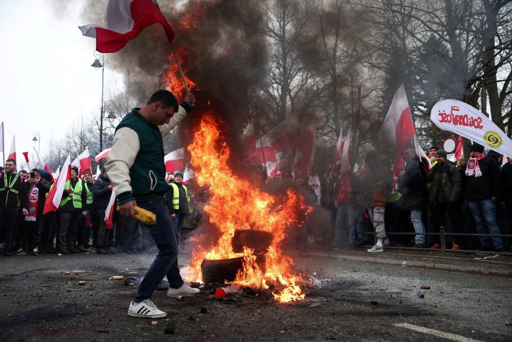 A man carries a Polish flag next to burning tyres, as farmers protest outside Polish Prime Minister Donald Tusk’s office against the European Union’s Green Deal and imports of Ukrainian agricultural products, in Warsaw, Poland, March 6, 2024. REUTERS/Kacper Pempel 
