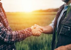 Two men shaking hands with a large field in the background.