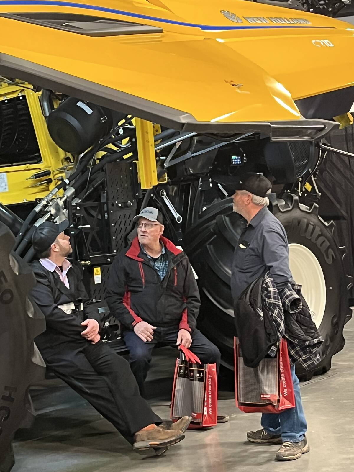 Agricultural producers take a break from the hustle and bustle of Lethbridge Ag Expo 2026, seeking shelter near the undercarriage of a huge New Holland CR1O combine. Photo: Greg Price