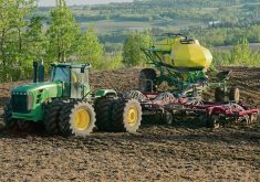 A green tractor pulling a large yellow air seeder across a dark cultivated field, illustrating nitrogen fertilizer application on the Prairies. Photo: Robin Booker
