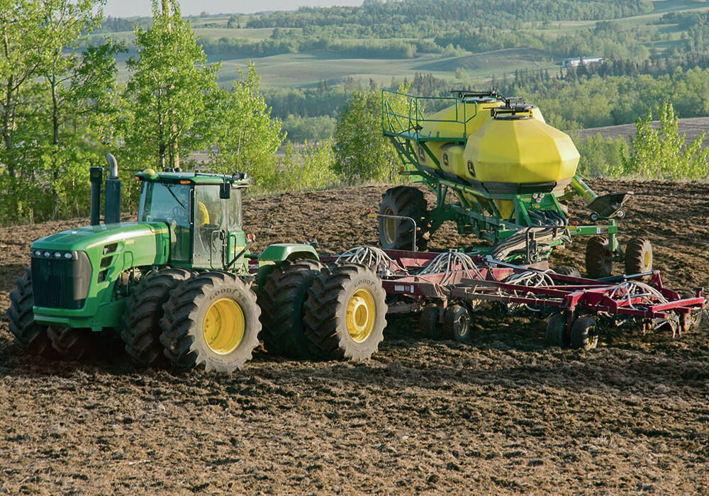 A green tractor pulling a large yellow air seeder across a dark cultivated field, illustrating nitrogen fertilizer application on the Prairies. Photo: Robin Booker