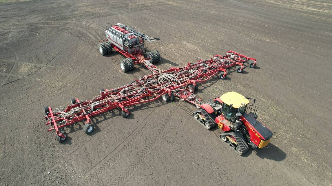 Aerial view of the Morris Quantum 100-foot air seeder fully extended in a bare field, paired with a Morris 10 Series 1440-bushel air cart and a red tracked tractor. The seeder, aimed at crop producers farming around 9,000 acres, is scheduled for full commercial release in 2027. Photo: Superior Farms Equipment