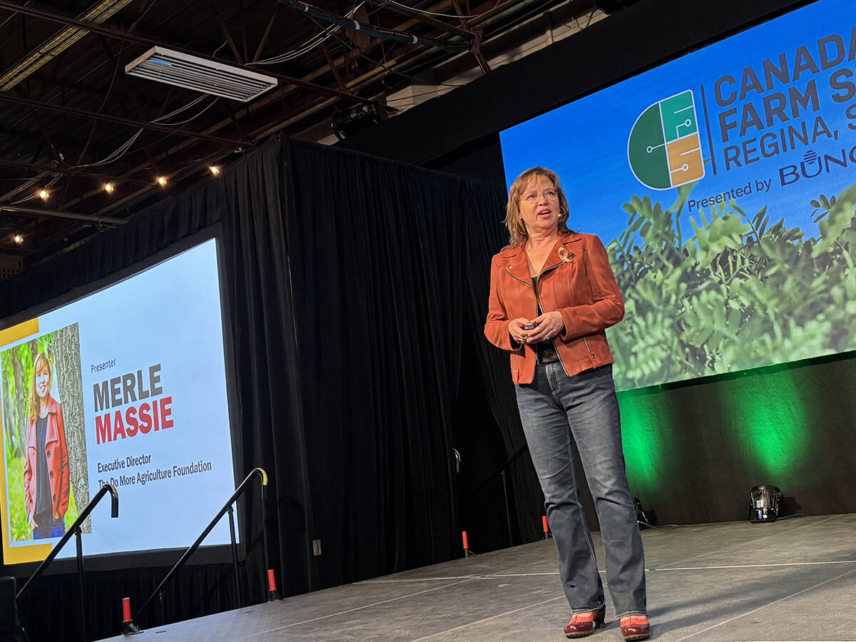 Merle Massie, executive director of DoMoreAg, speaks on stage at Canada's Farm Show in Regina about AgTalk, an anonymous peer support platform for farmers. The presentation screen behind her displays her name and title. Photo: Karen Briere