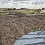 Rows of manure compost arranged in windrows inside a corral on Claude Lampron's farm near Saint Vincent, Alta., with farmyard buildings and green fields visible in the background. Photo: Claude Lampron