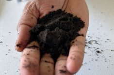 A hand holding a clump of dark soil against a light surface. The federal government has announced a partnership with the Soil Conservation Council of Canada to develop a National Agricultural Soil Health Strategy. Photo: Don Norman