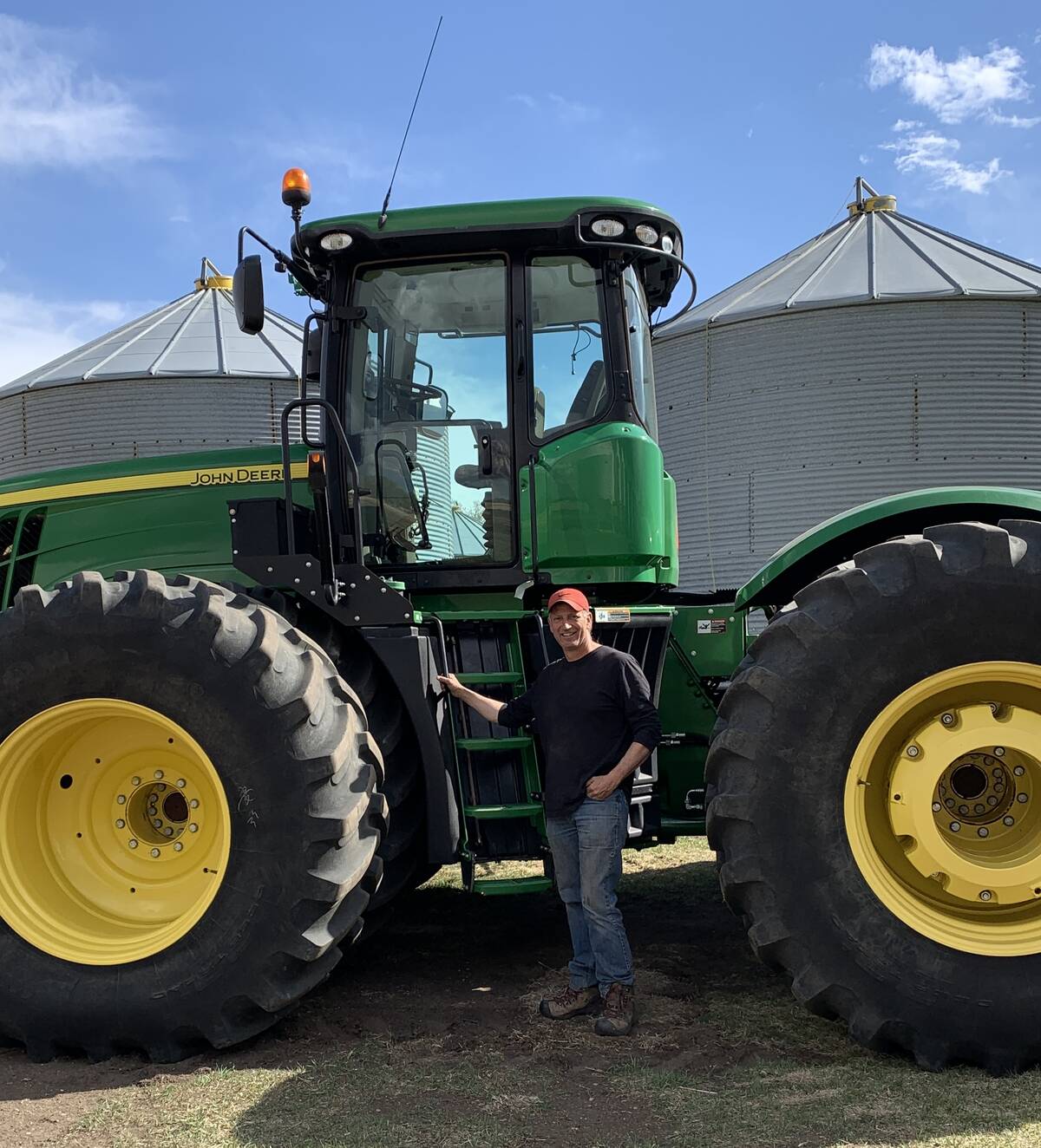 Roger Chevraux, a grain farmer from Killam, standing beside a green John Deere tractor with grain bins in the background. Chevraux sees the national soil health strategy as a positive step for Canadian agriculture. Photo: supplied