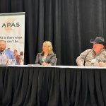 Chris Procyk, Adrienne Ivey and Trevor Green sit behind microphones at a draped panel table during the Agricultural Producers Association of Saskatchewan Policy Summit, with APAS signage behind them. Photo: Janelle Rudolph
