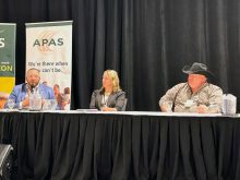 Chris Procyk, Adrienne Ivey and Trevor Green sit behind microphones at a draped panel table during the Agricultural Producers Association of Saskatchewan Policy Summit, with APAS signage behind them. Photo: Janelle Rudolph