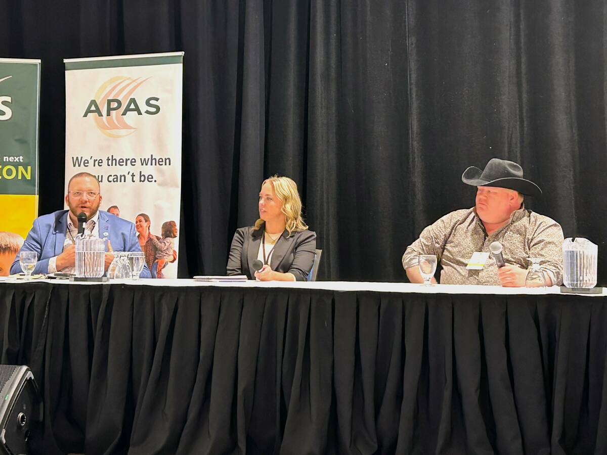 Chris Procyk, Adrienne Ivey and Trevor Green sit behind microphones at a draped panel table during the Agricultural Producers Association of Saskatchewan Policy Summit, with APAS signage behind them. Photo: Janelle Rudolph
