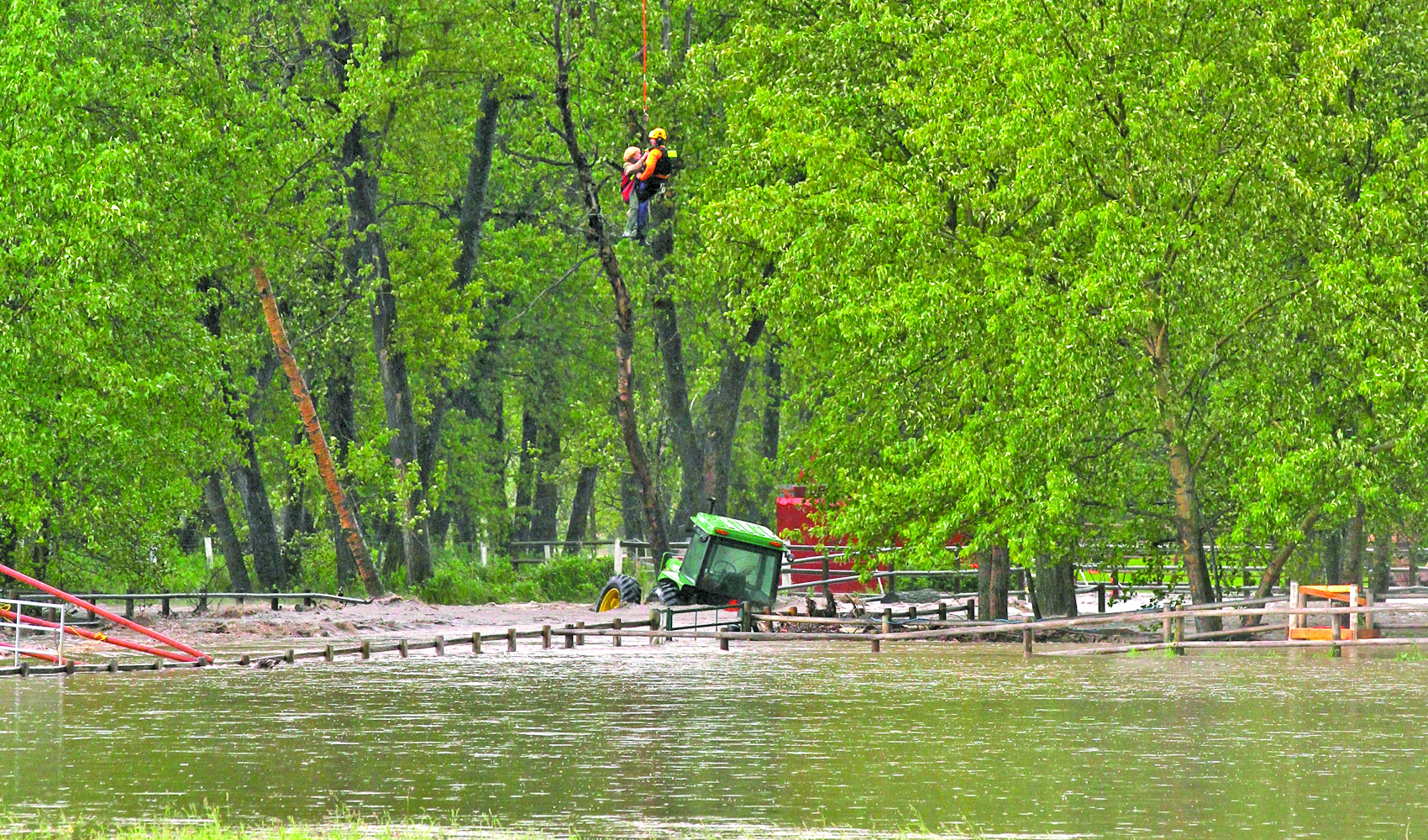 A woman is airlifted by helicopter from a flooded farm near Millarville, Alta., with a tractor partially submerged by floodwaters from Three Point Creek. Photo: Wendy Dudley