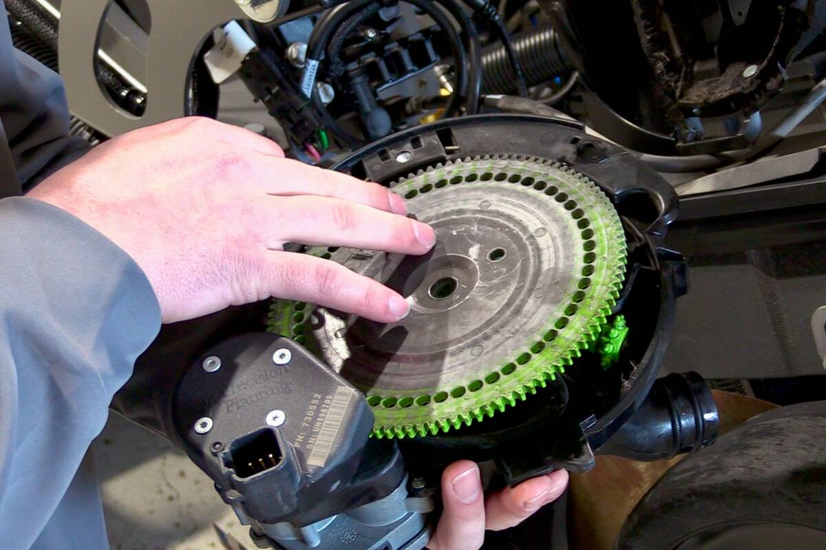Close-up of hands inspecting a seed disc on a planter row unit, showing the green-toothed meter disc and surrounding components. Photo: Greg Berg